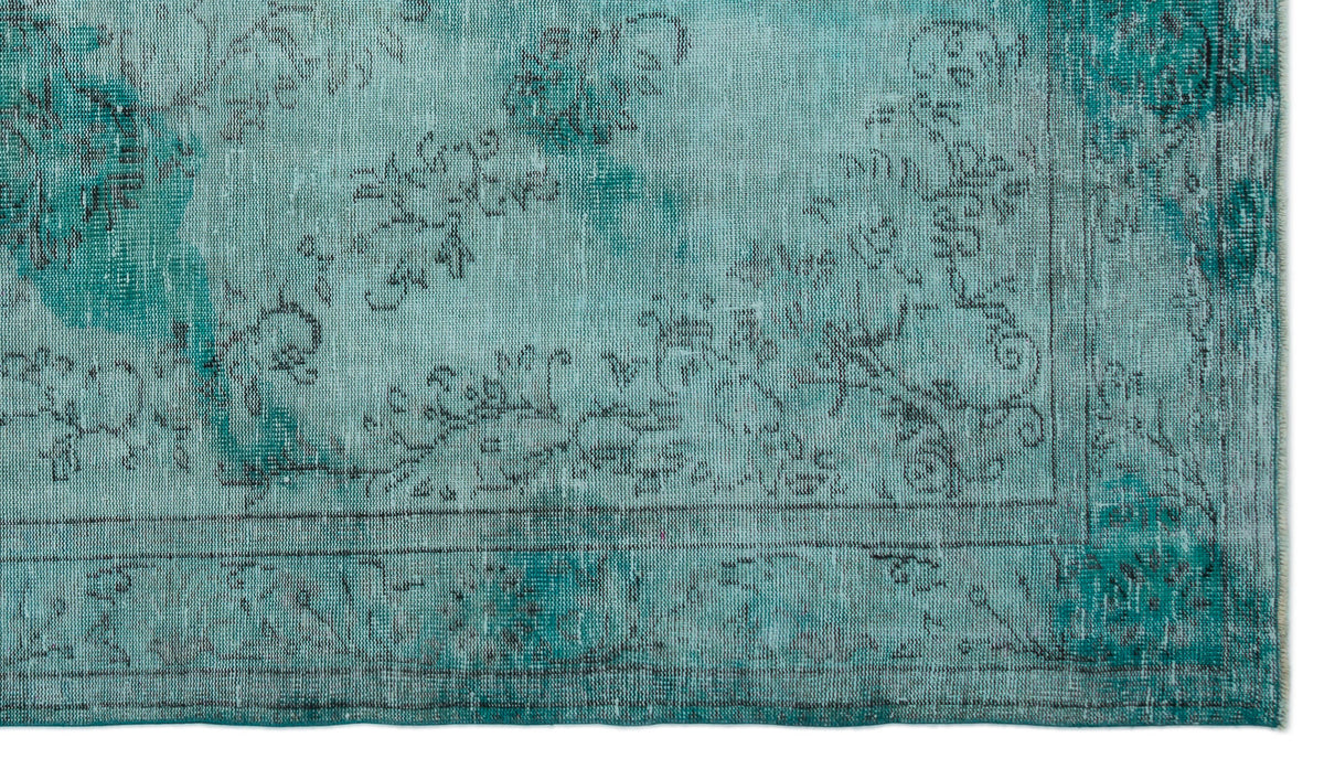 Teal and turquoise distressed rug with a faded black floral medallion pattern and a bordered edge.