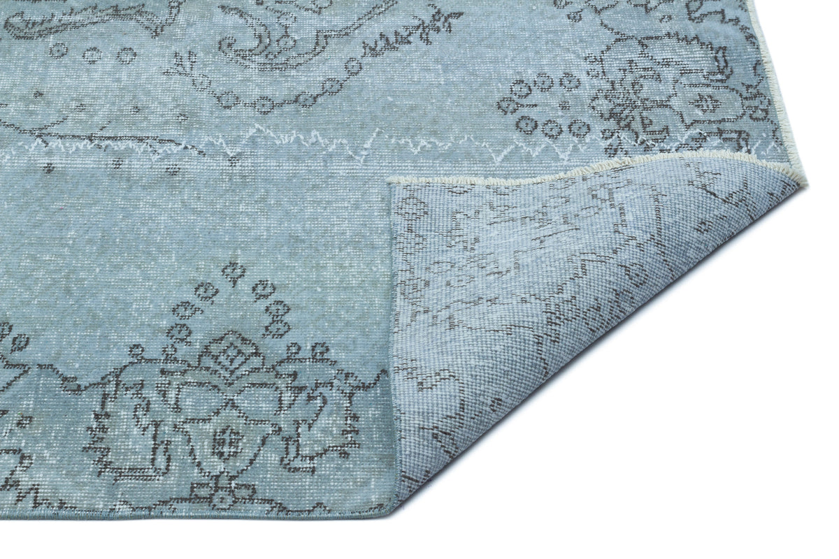 Light blue distressed rug with a dark grey floral medallion pattern and a folded corner showing the backing.