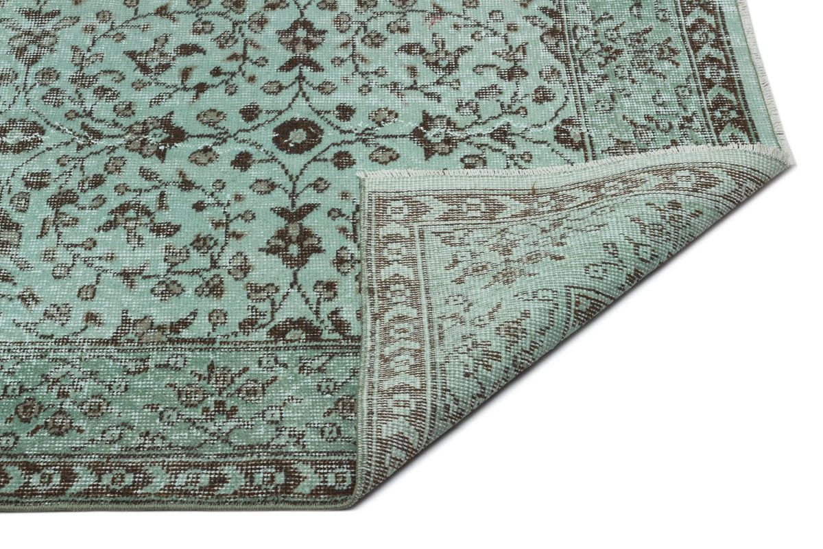 Mint green and brown traditional rug with a floral medallion pattern and a folded corner, isolated on white.