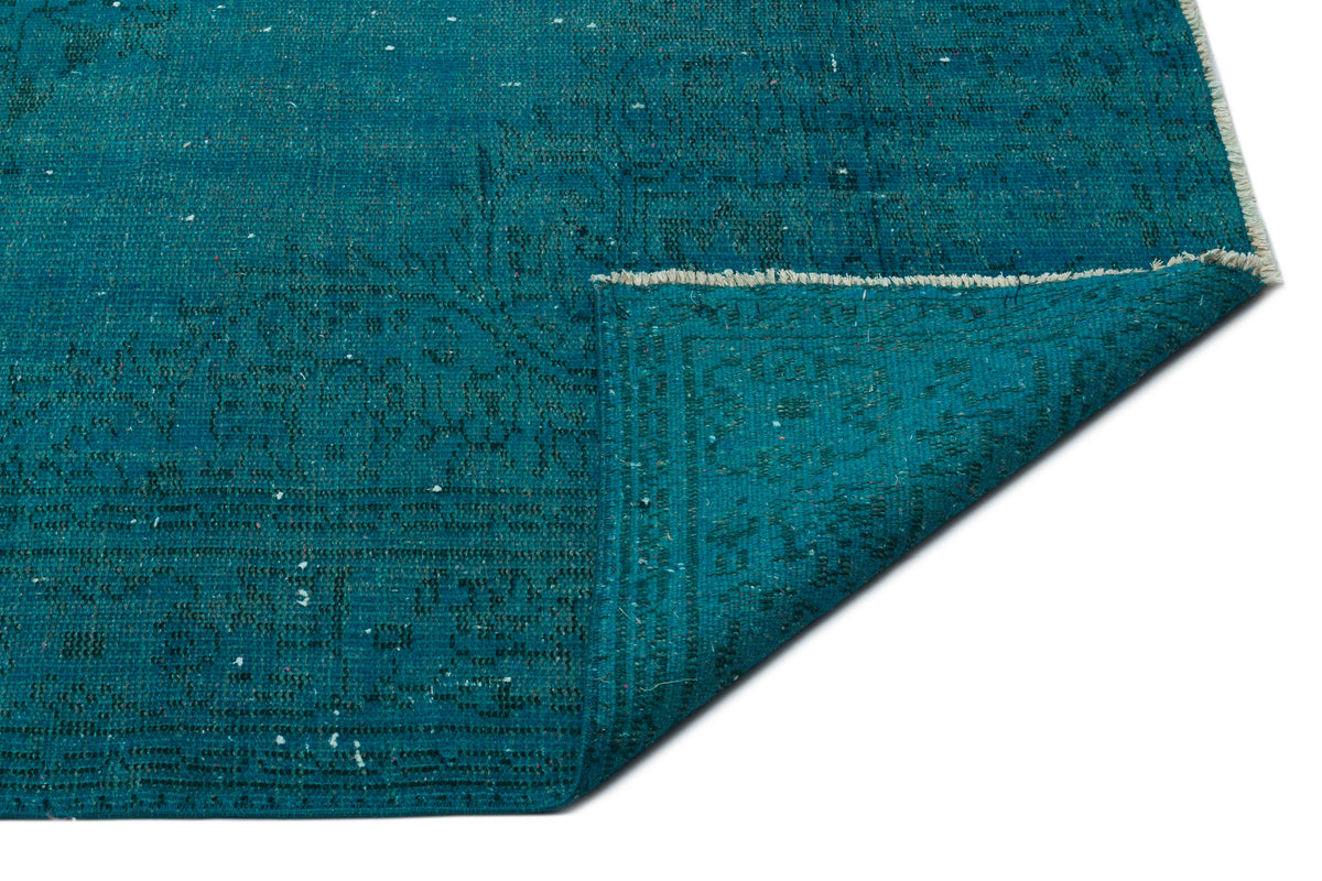 Teal distressed rug with a faded traditional pattern and a folded corner showing the underside and fringe.