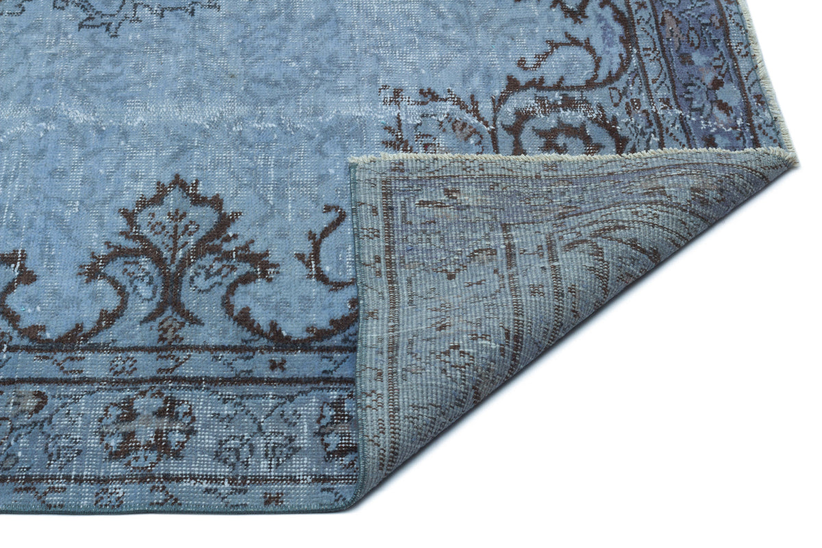Distressed light blue rug with dark brown floral medallion patterns, shown with a corner folded over on a white background.