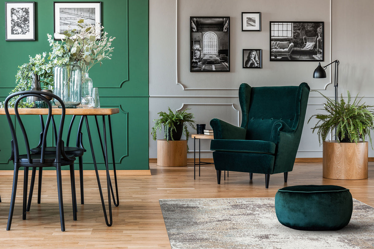 Grey and beige distressed abstract rug in a living room with green velvet furniture and wood flooring.