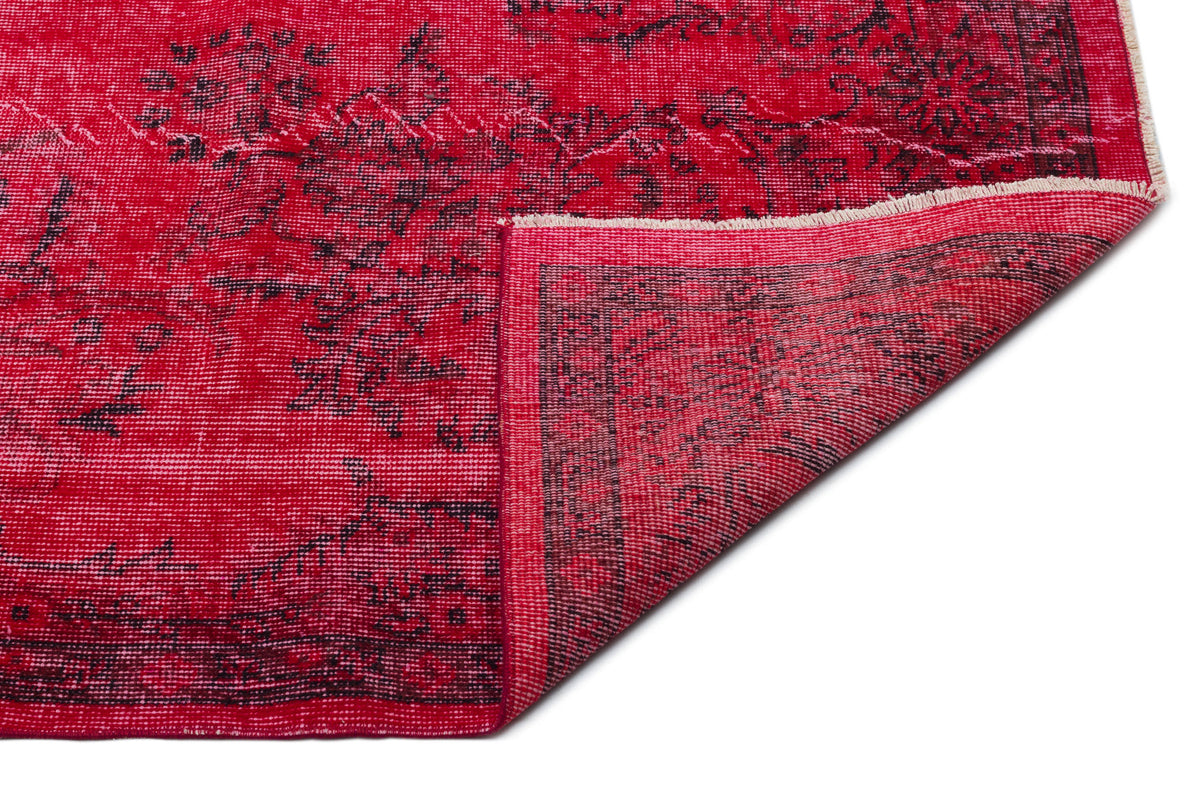 Vibrant red rug with a distressed black floral pattern and a folded corner showing the woven backing.