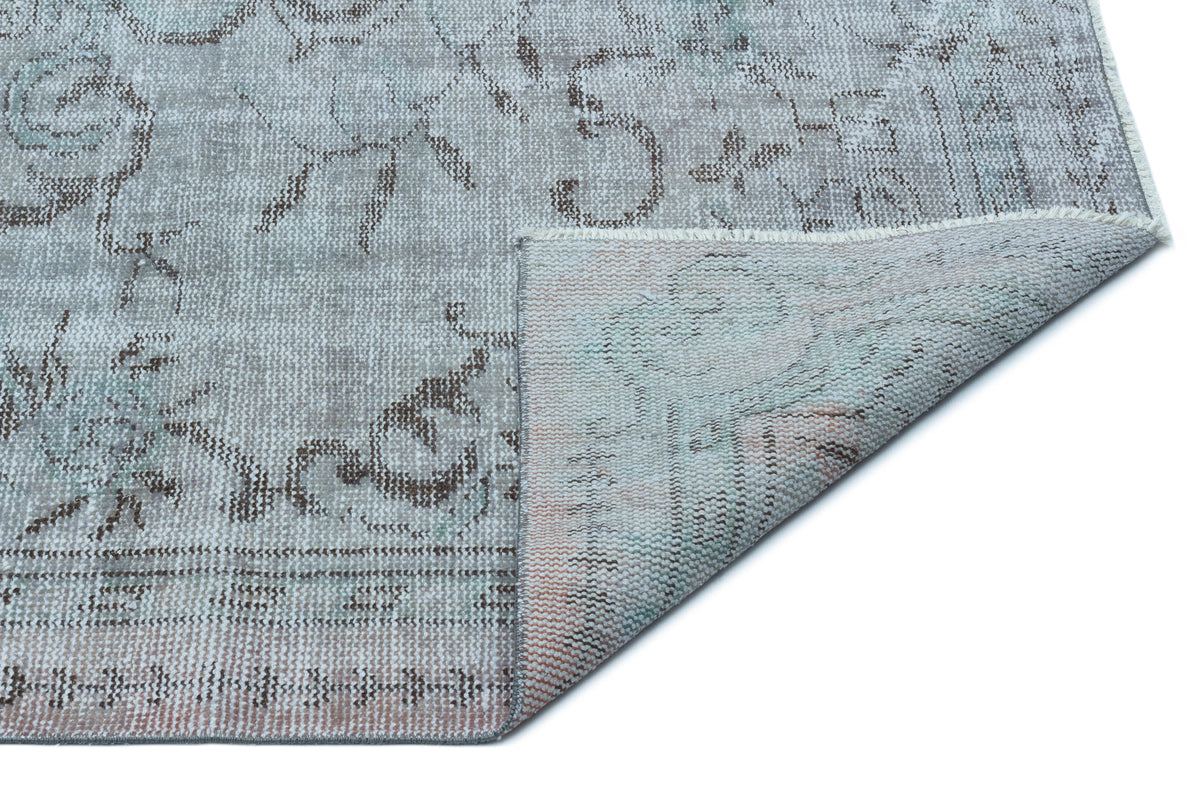 Grey and beige distressed floral rug with a folded corner revealing the woven backing.