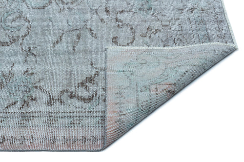 Load image 1 in gallery view. Grey and beige distressed floral rug with a folded corner revealing the woven backing.