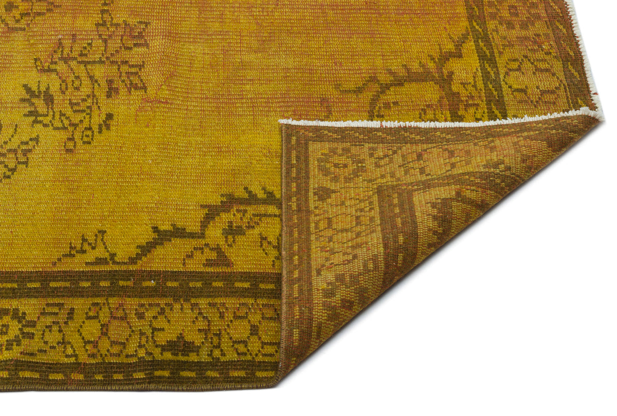 Mustard yellow and brown distressed rug with a traditional floral border and corner fold, isolated on white.