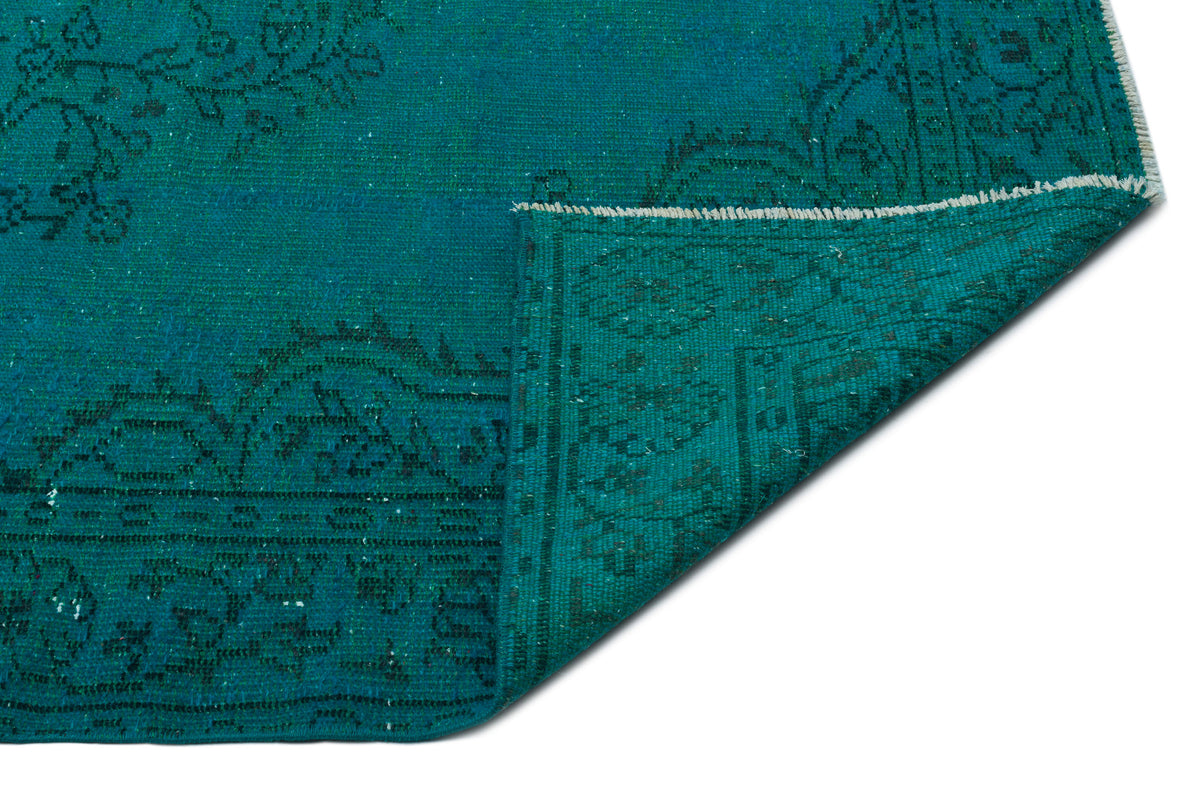 Teal rug with a dark green traditional floral pattern, shown with a corner folded over on a white background.