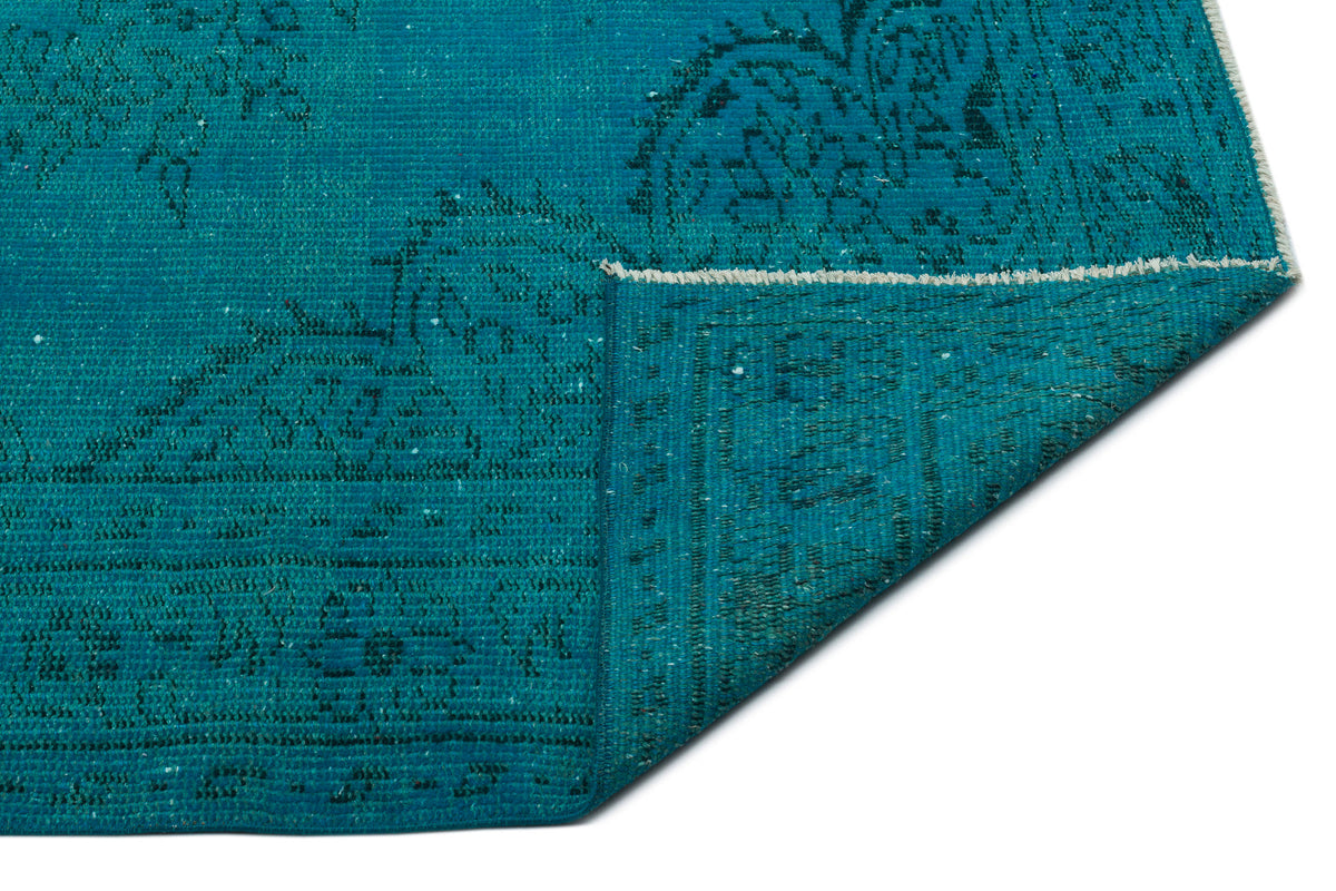 Teal rug with a distressed traditional medallion pattern, shown with a corner folded over on a white background.
