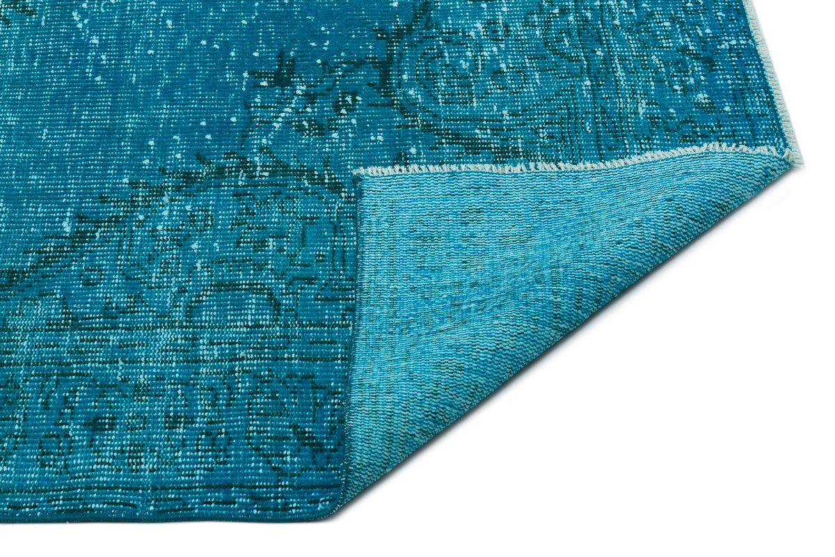 Teal distressed rug with a faded traditional medallion pattern, shown with a corner folded over to reveal the backing.