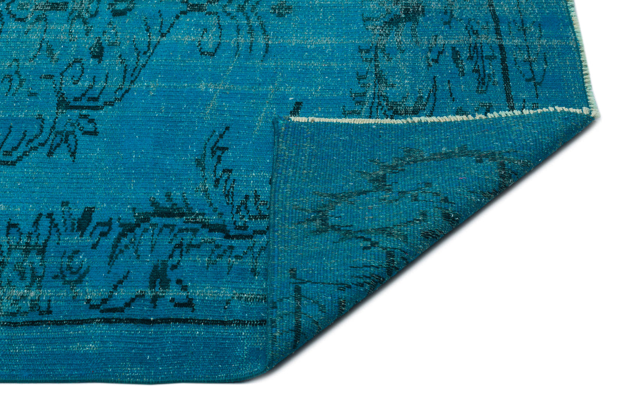 Bright blue rug with a distressed black traditional pattern and a folded corner revealing the underside.