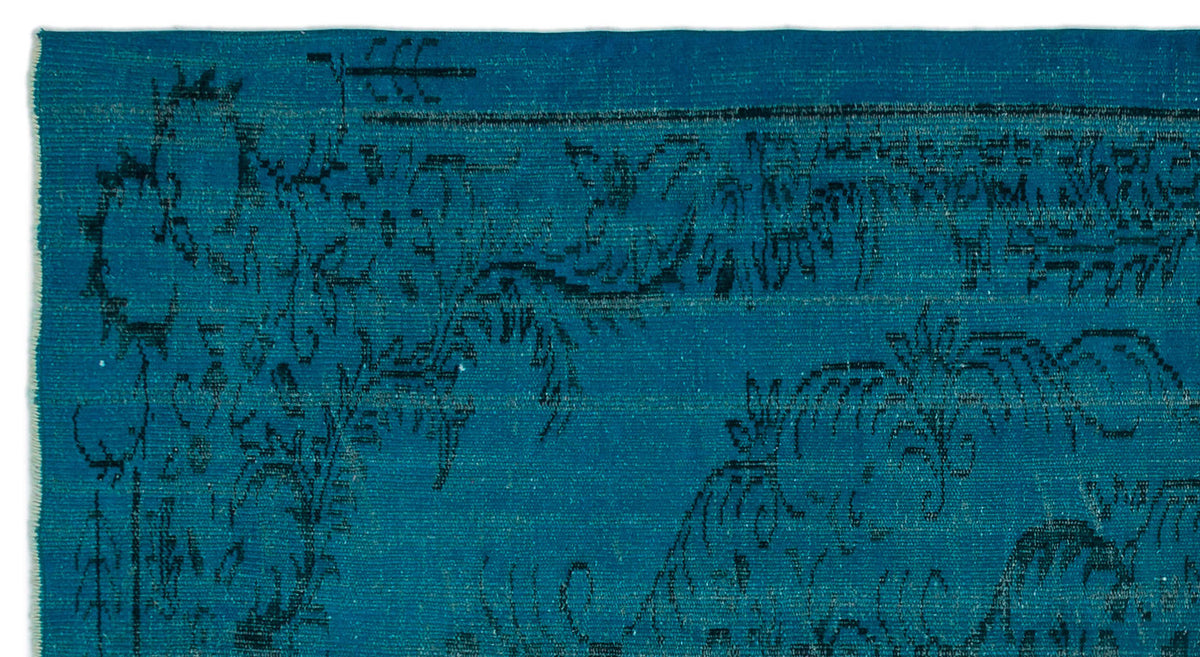 Teal rug with a distressed black floral and vine pattern.