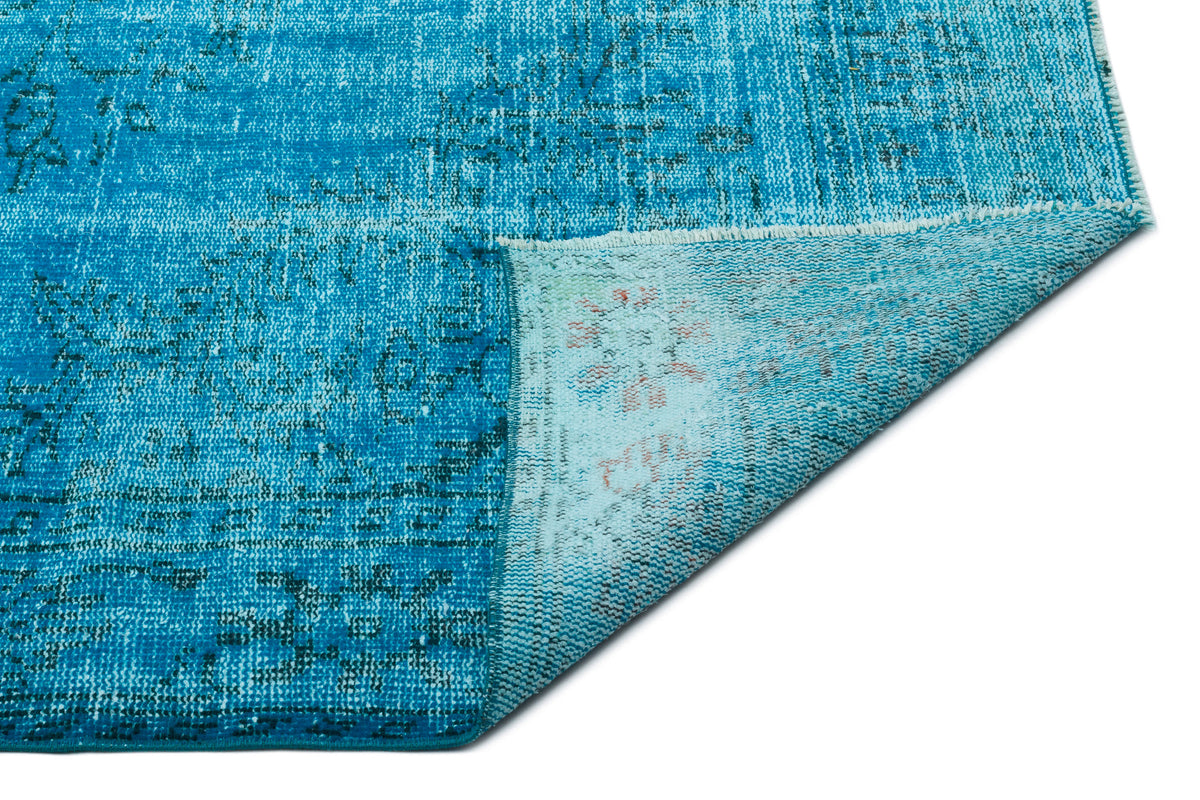 Bright blue distressed rug with a faded traditional pattern, shown with a corner folded over to reveal the backing.