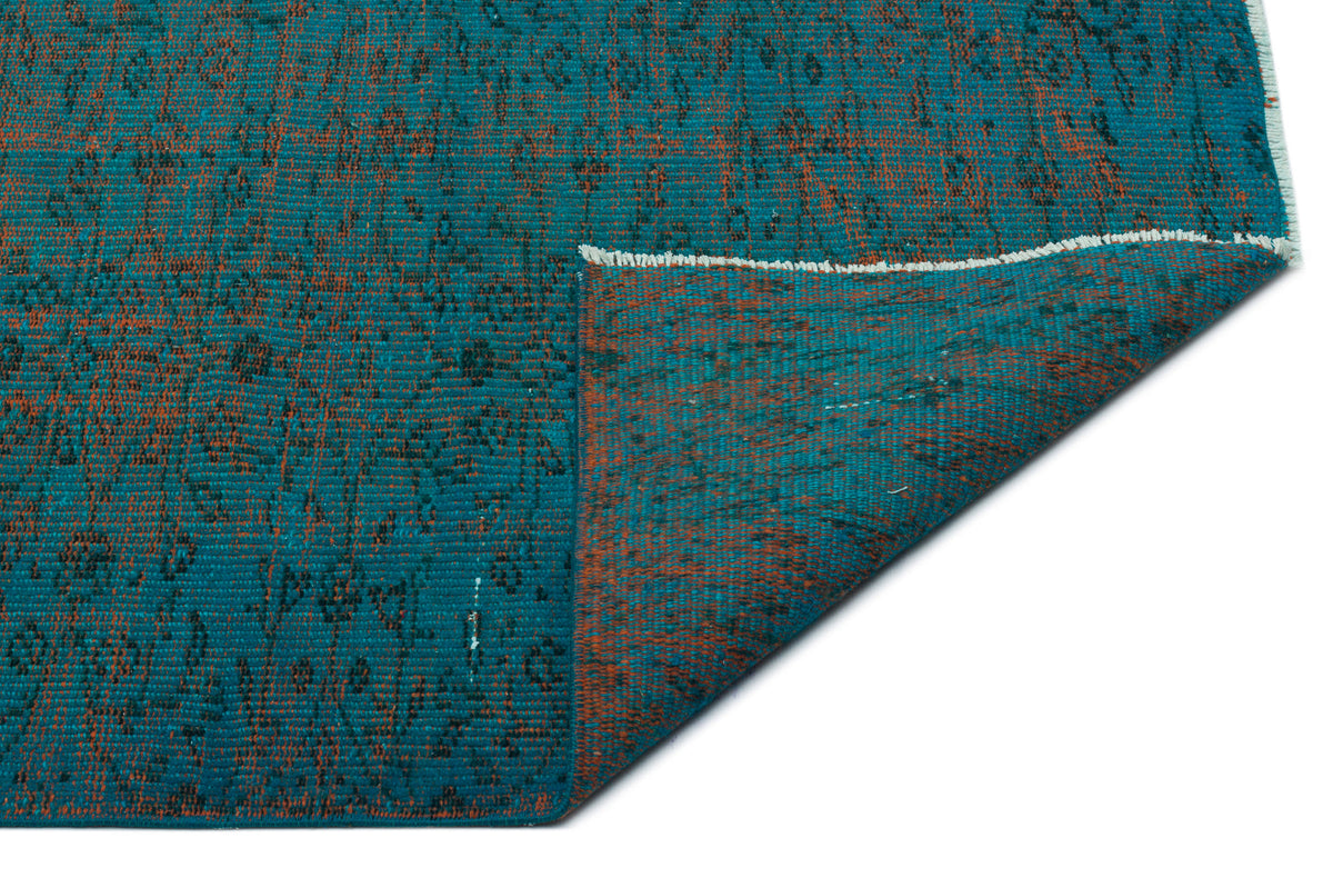 Teal and rust-orange distressed rug with a faded traditional pattern, shown with a corner folded over on a white background.