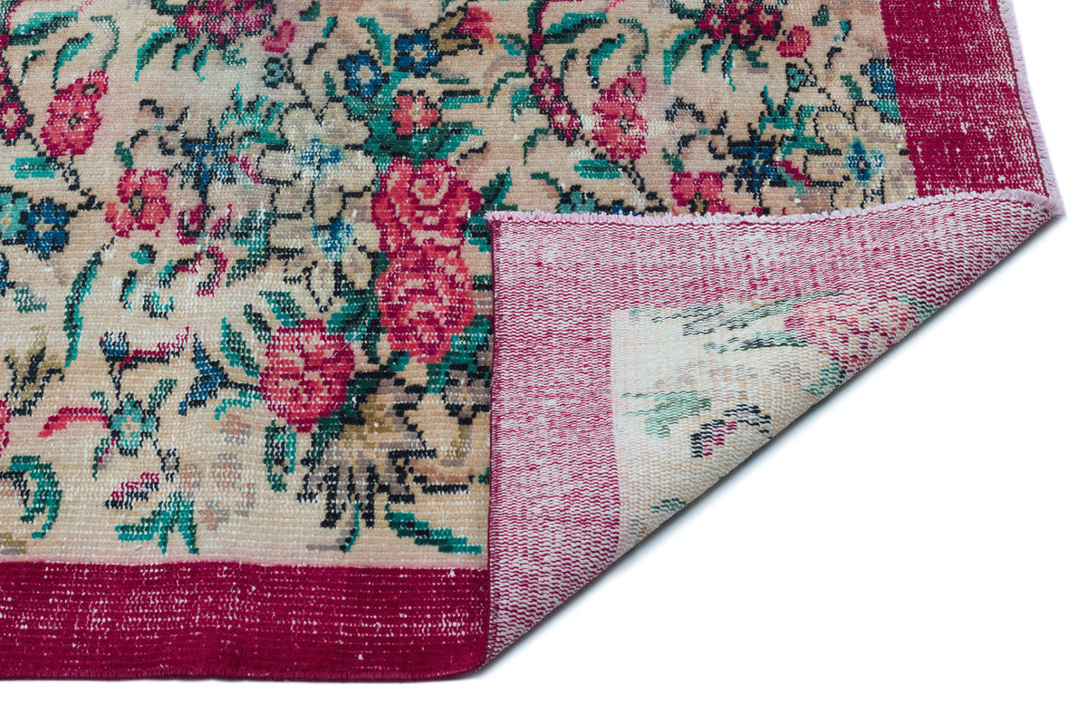 Beige rug with a distressed floral pattern in pink, teal, and black, featuring a wide magenta border and folded corner.