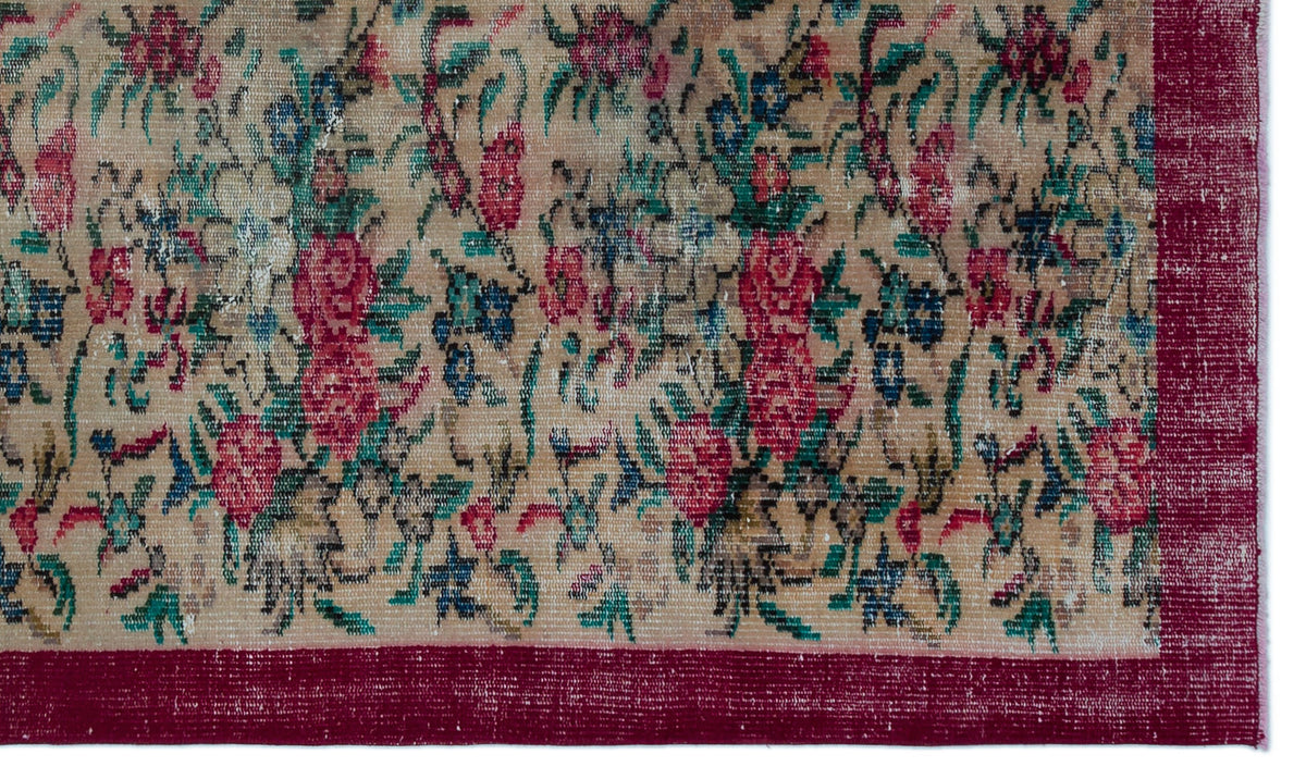 Beige rug with a distressed floral pattern in red, blue, and green, featuring a solid dark red border.