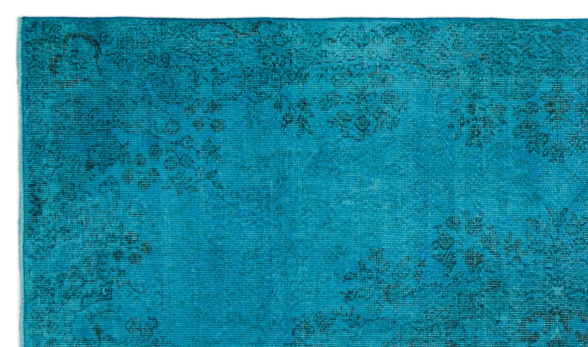 Bright turquoise rug with a faded black floral medallion pattern and distressed texture.