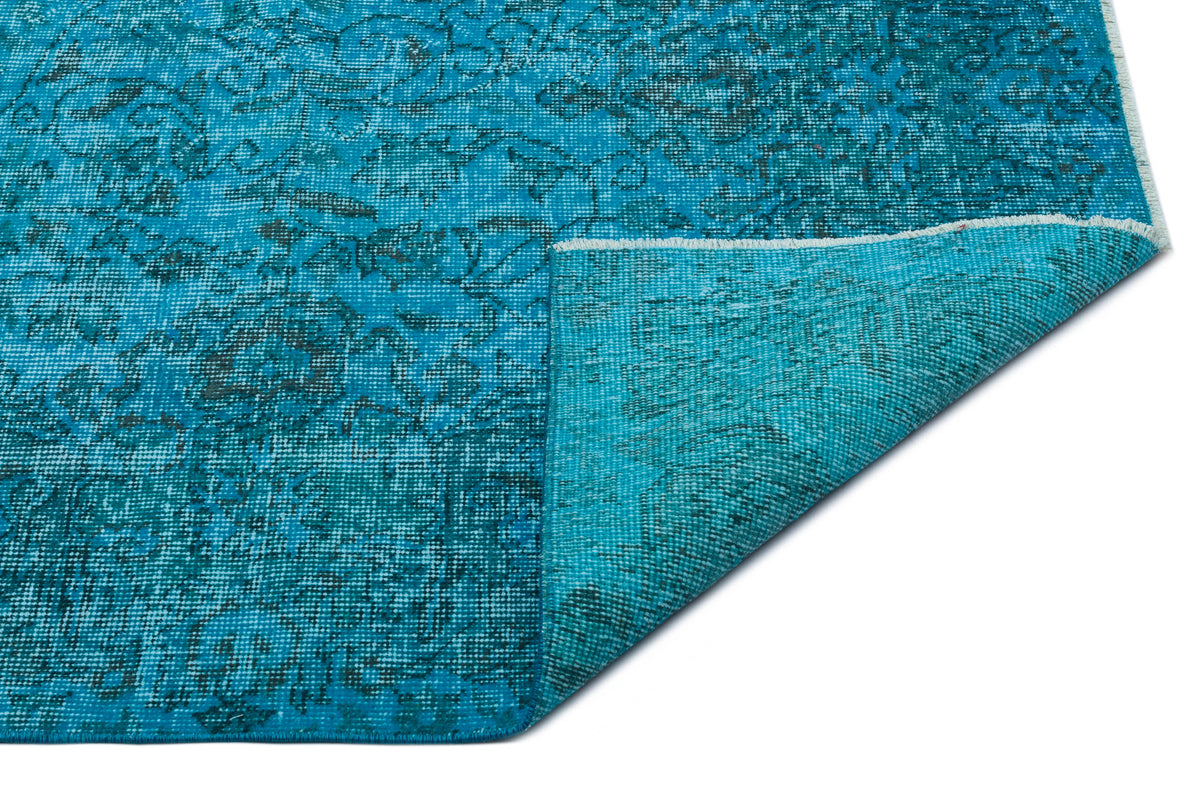 Bright turquoise rug with a distressed floral pattern and a folded corner revealing the woven backing.