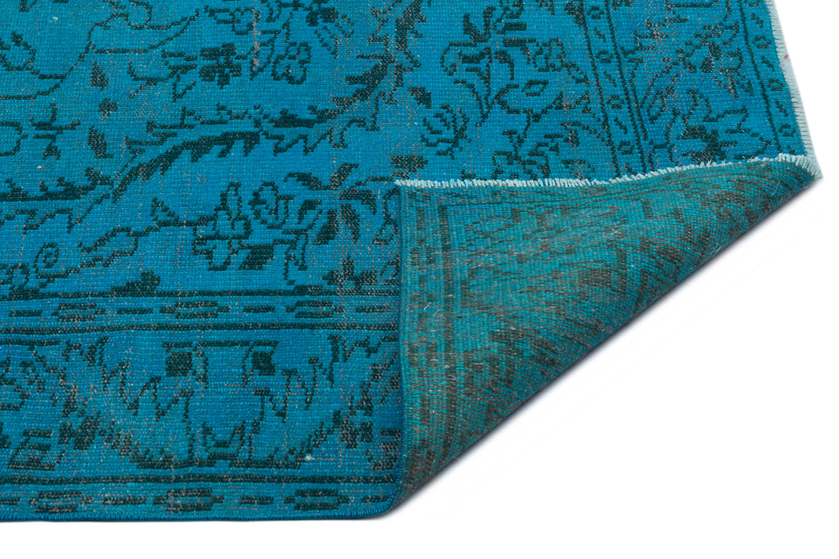 Bright turquoise rug with a dark charcoal floral pattern and a folded corner revealing the underside.