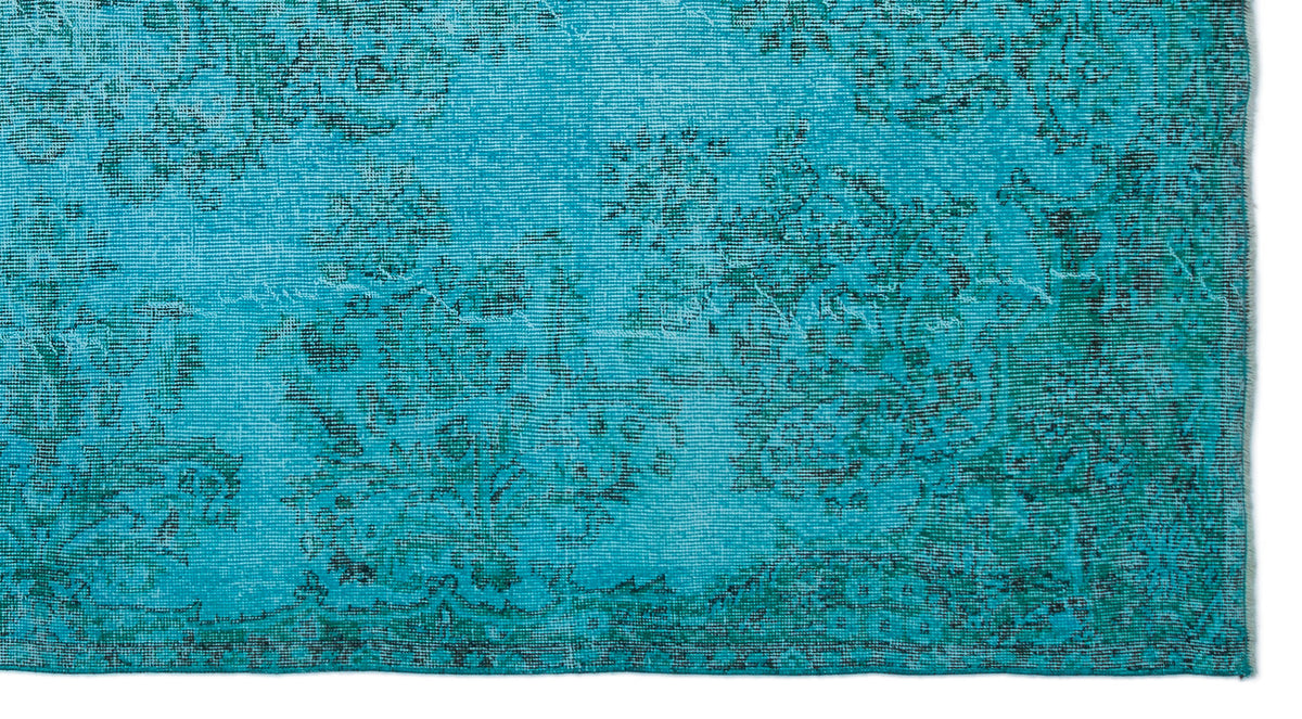 Bright turquoise rug with a distressed, dark green floral medallion pattern on a white background.