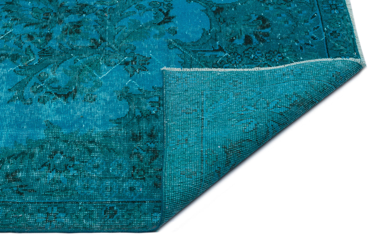 Teal distressed rug with a dark floral medallion pattern and a folded corner showing the woven backing.