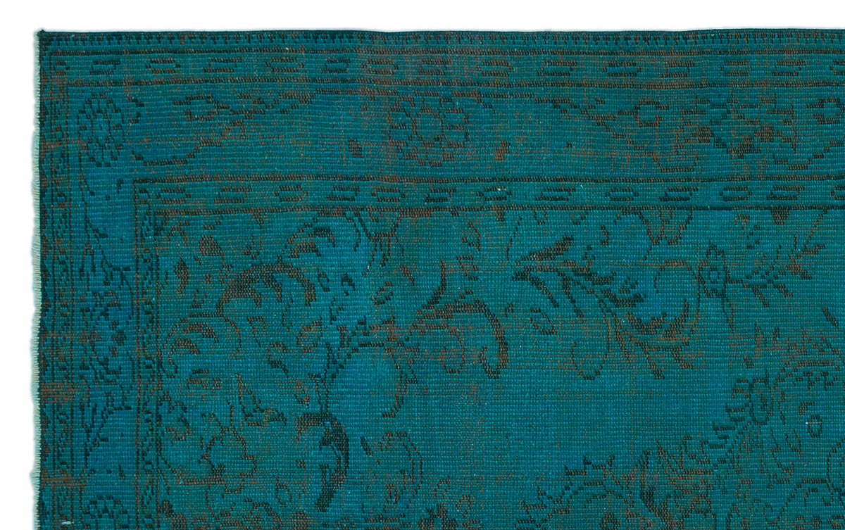 Teal rug with a dark brown distressed floral pattern and a geometric border.