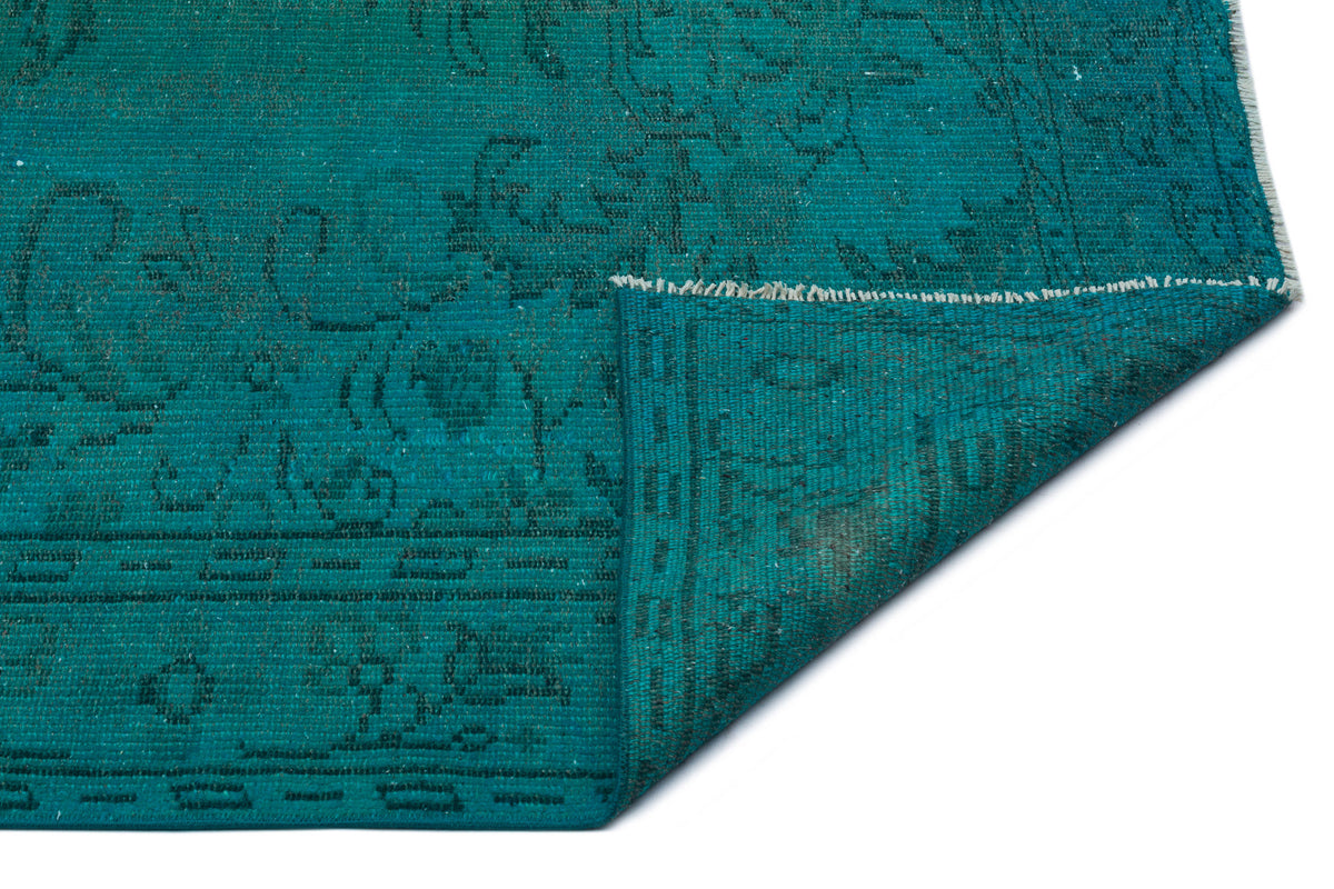 Teal rug with a dark, distressed traditional pattern and a folded corner showing the underside on a white background.