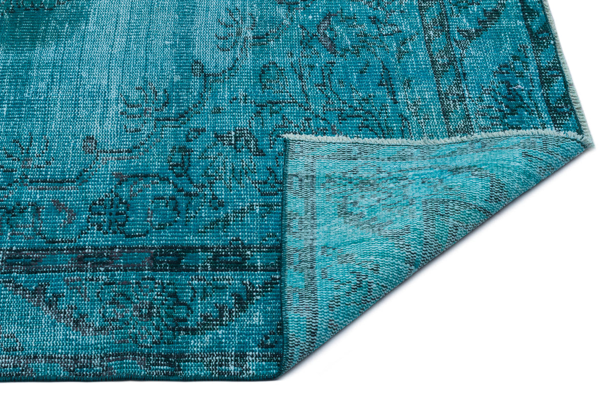 Teal distressed rug with a dark floral medallion pattern, shown with a corner folded over on a white background.