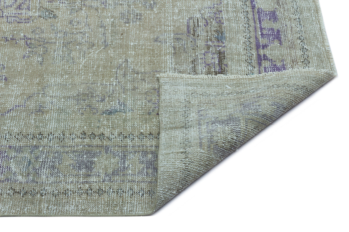 Beige and purple distressed vintage-style rug with a folded corner showing the woven backing.