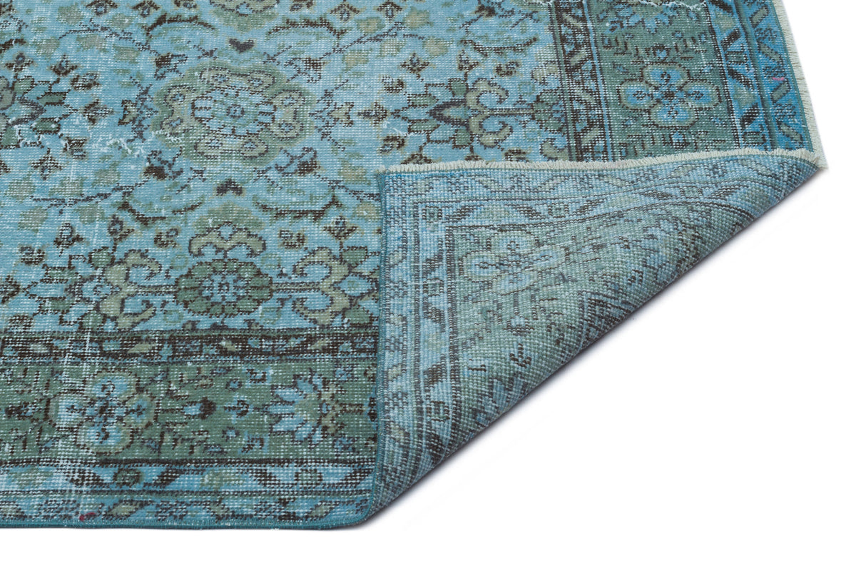 Distressed turquoise and sage green traditional rug with a floral medallion pattern, shown with a folded corner.