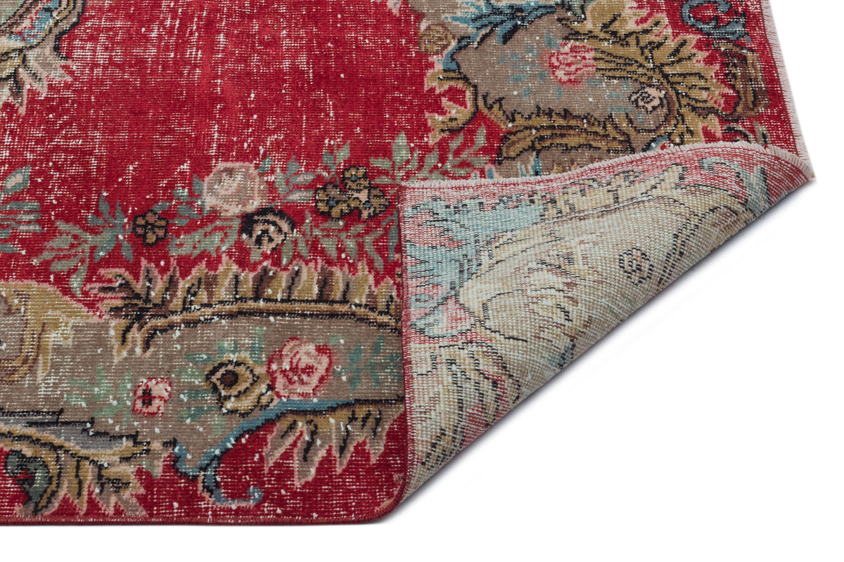 Distressed red rug with a floral medallion pattern and a folded corner revealing a light beige underside.