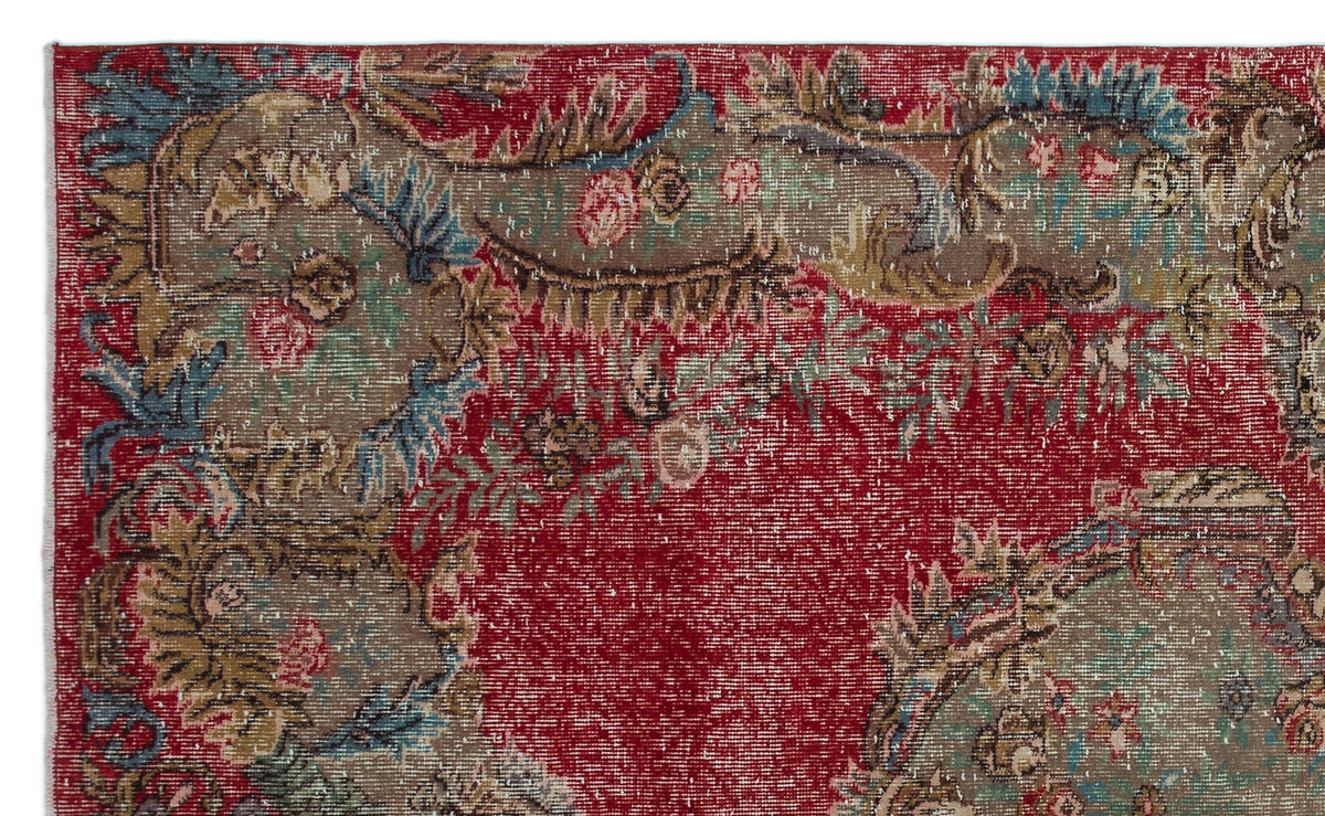 Distressed red rug with a faded floral medallion pattern in muted blue, green, and beige tones.