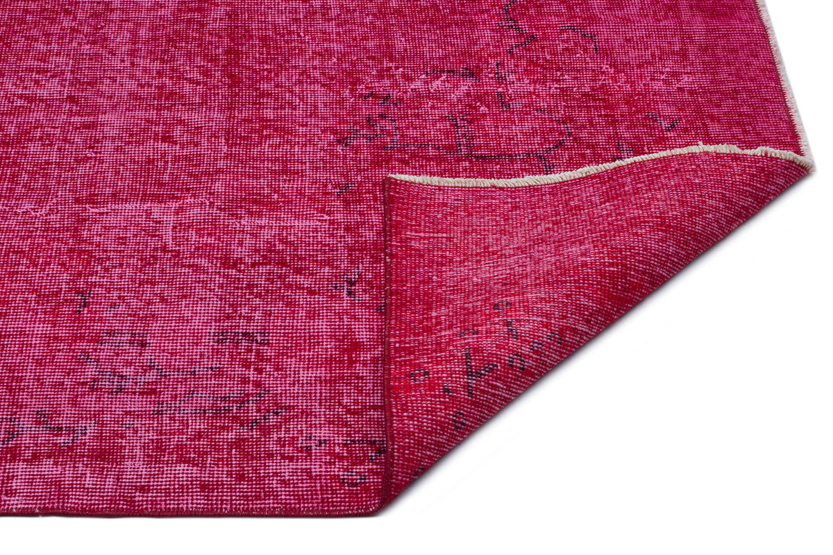 Magenta distressed rug with a faded traditional pattern and a folded corner, isolated on a white background.