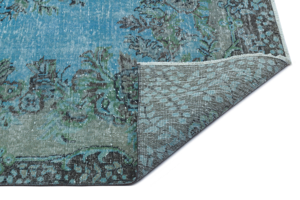 Distressed blue and grey rug with a floral pattern, shown with a corner folded to reveal the woven backing.
