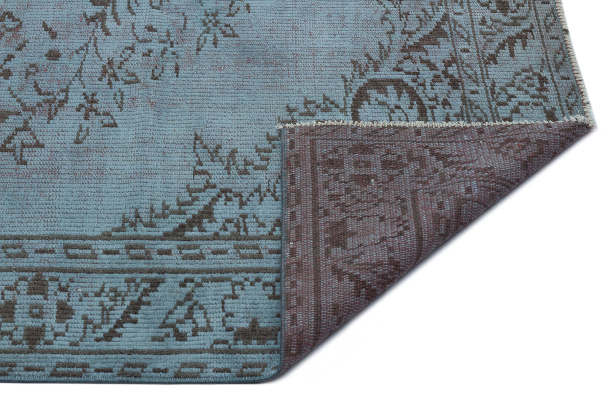 Light blue rug with a dark brown distressed floral pattern and a folded corner revealing the reverse side.