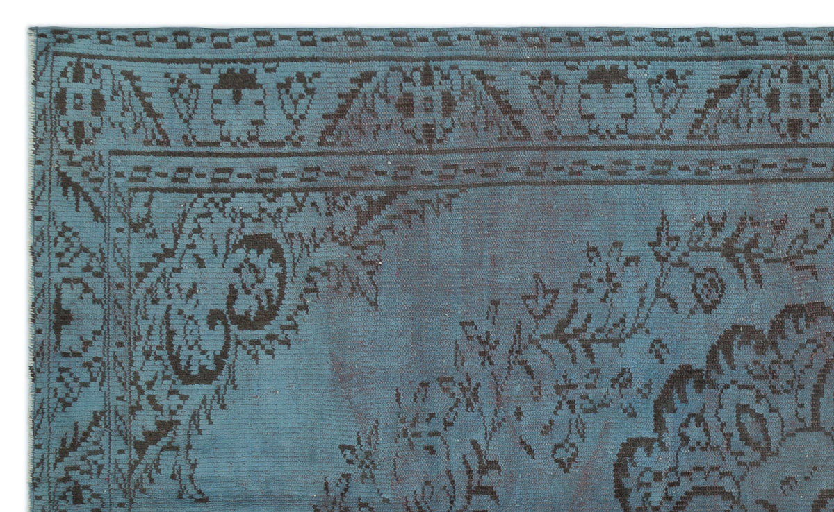 Teal rug with a dark brown distressed floral medallion pattern and a geometric border.