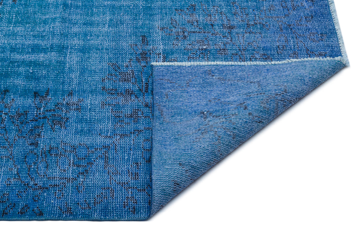 Blue distressed rug with a faded black floral pattern, shown with one corner folded over to reveal the backing.