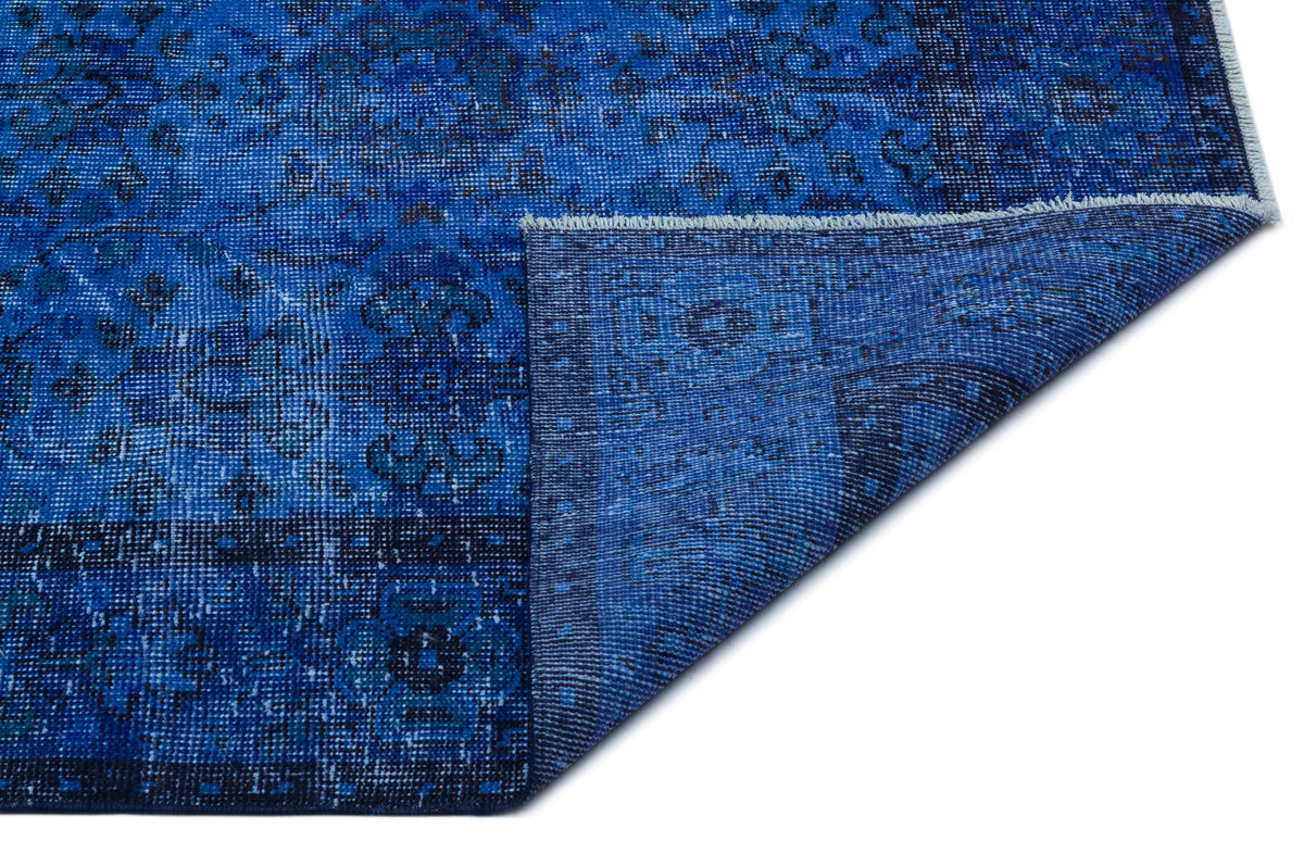Deep blue distressed rug with a traditional floral medallion pattern and a folded corner showing the underside.