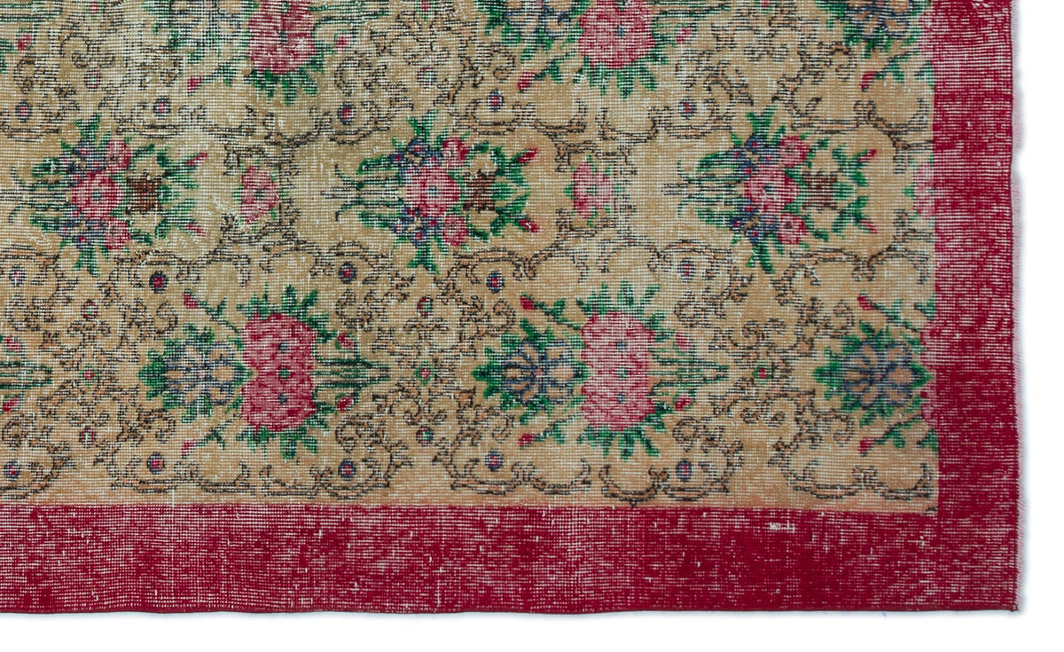 Tan rug with a repeating floral medallion pattern in pink, green, and blue, featuring a wide red border.