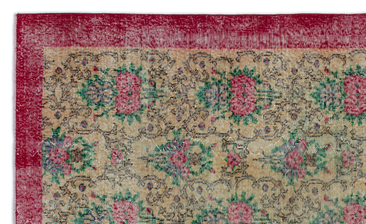 Distressed beige rug with a red border and repeating floral medallion pattern in pink, green, and dark blue.