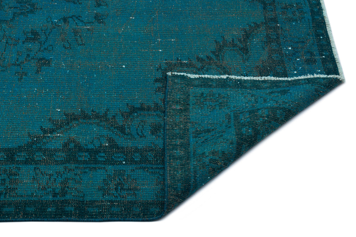 Teal and dark grey distressed rug with a traditional medallion pattern, shown with a folded corner on a white background.