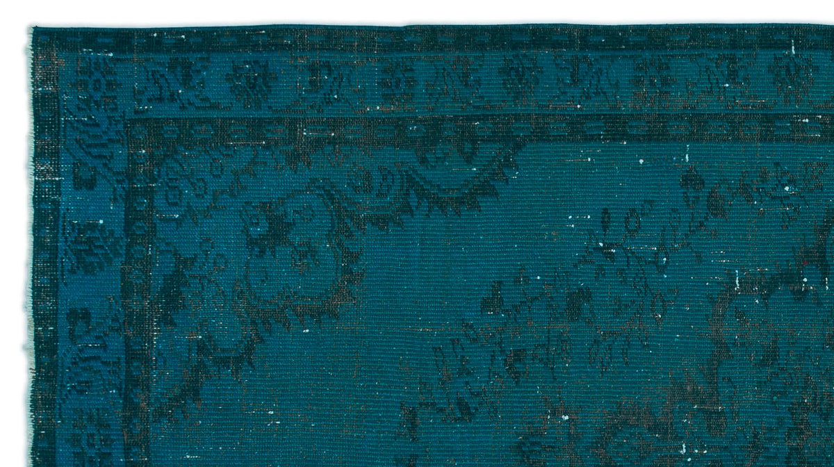 Teal rug with a distressed, dark floral medallion pattern and a geometric border.
