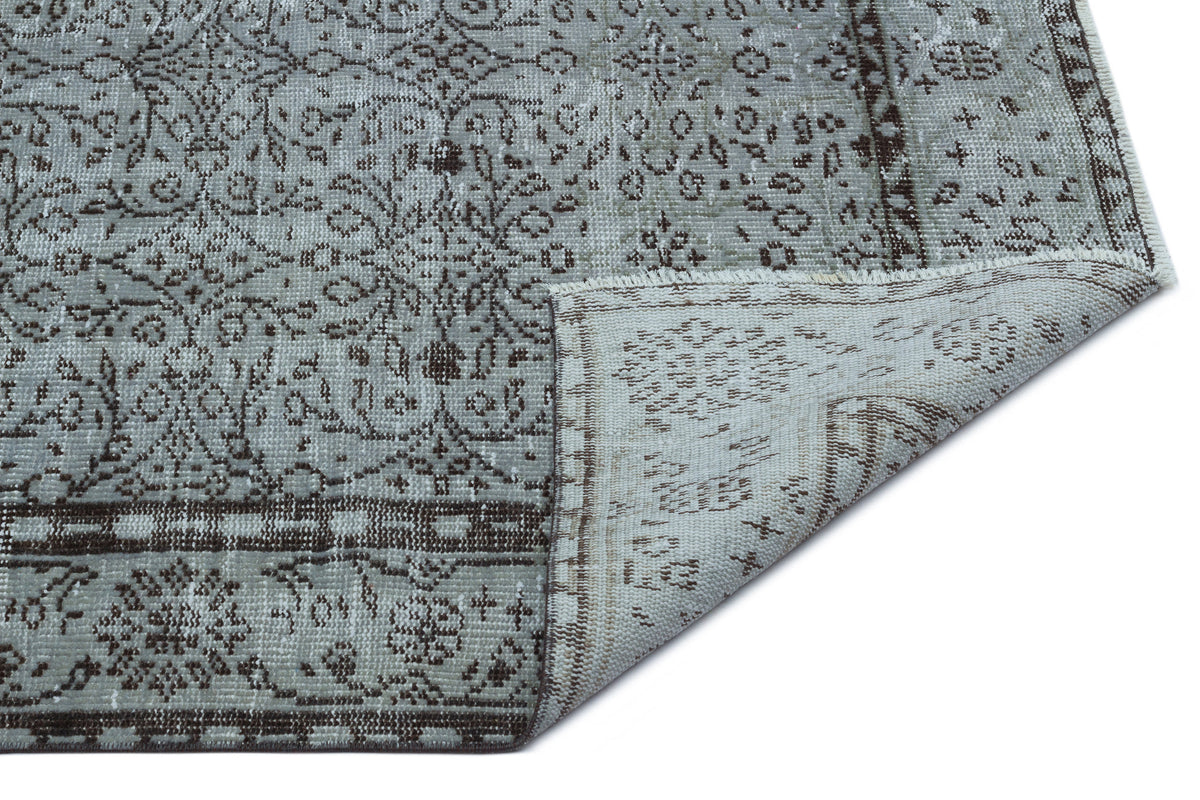 Grey and brown distressed rug with a traditional floral medallion pattern and a folded corner showing the backing.