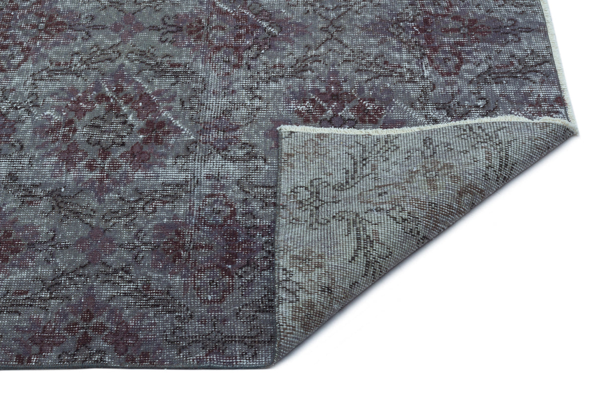 Grey and burgundy distressed medallion rug with a folded corner showing the woven backing on a white background.