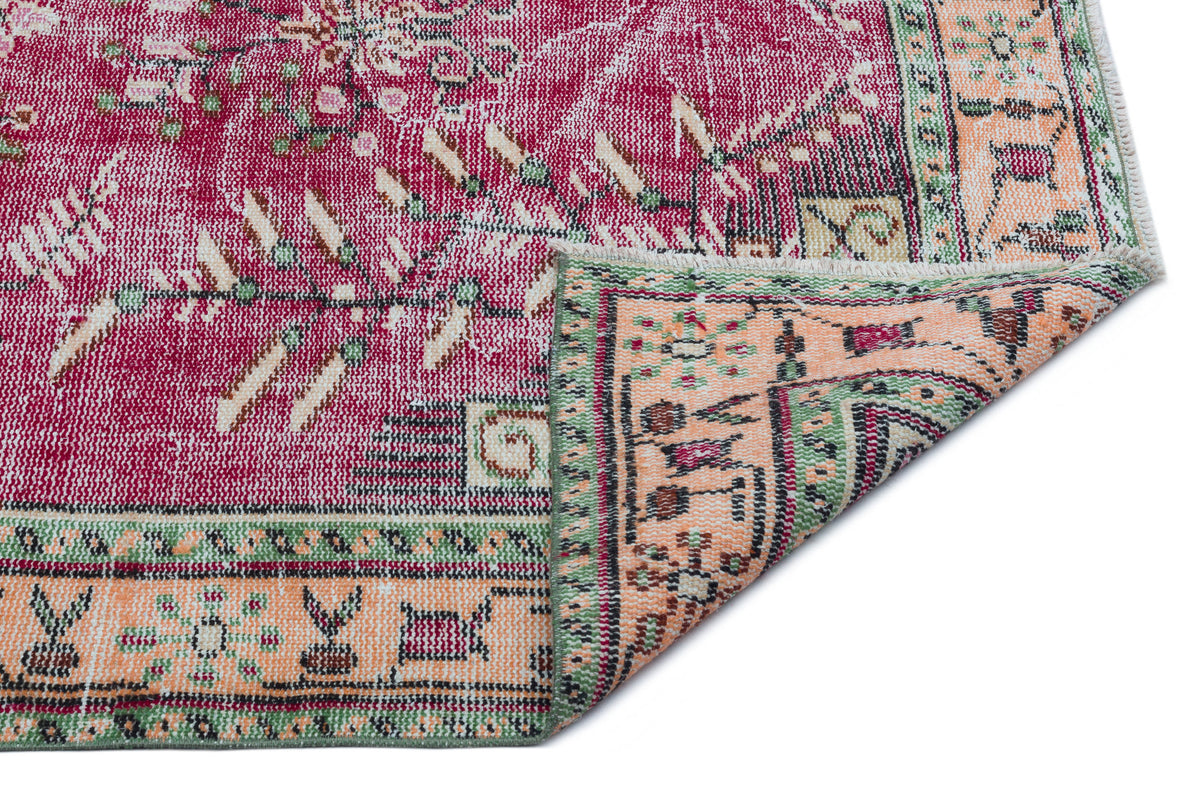 Distressed magenta, peach, and green rug with a traditional floral medallion pattern and a folded corner.