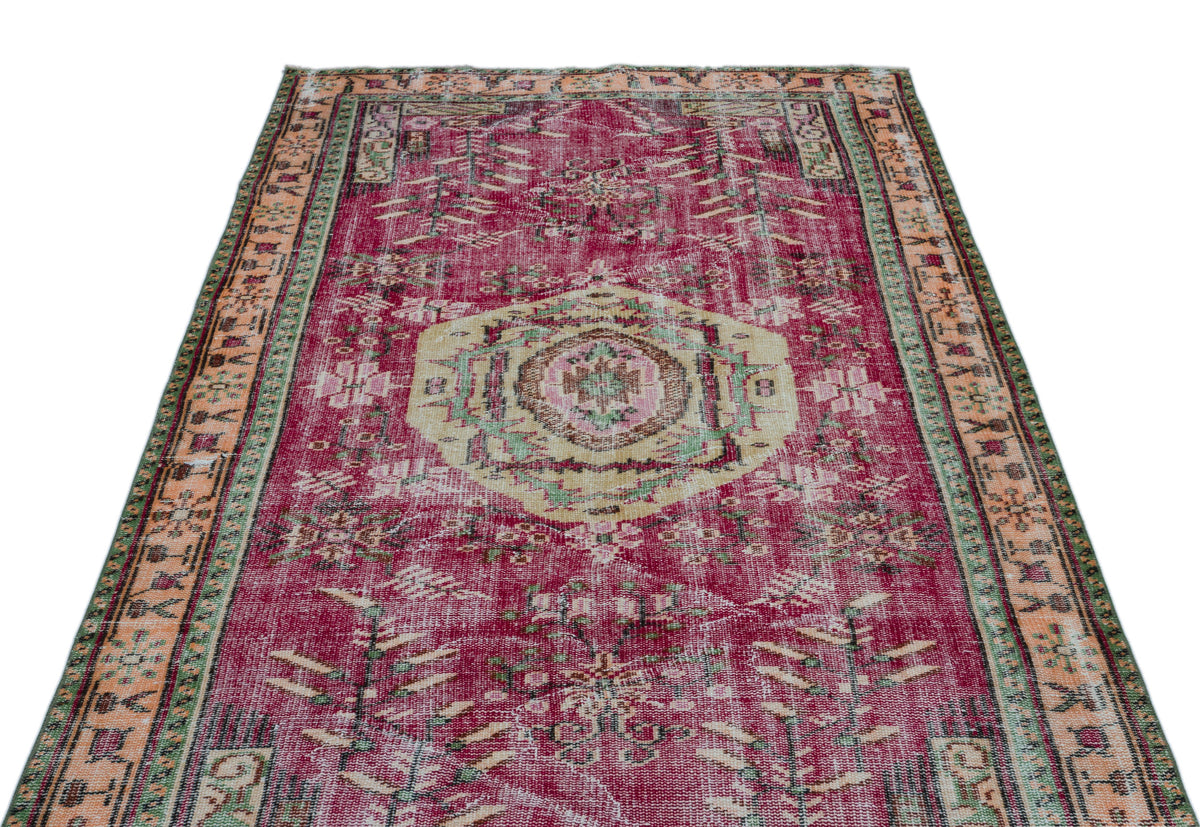 Distressed magenta vintage-style rug with a central beige medallion, geometric patterns, and a multi-colored border.