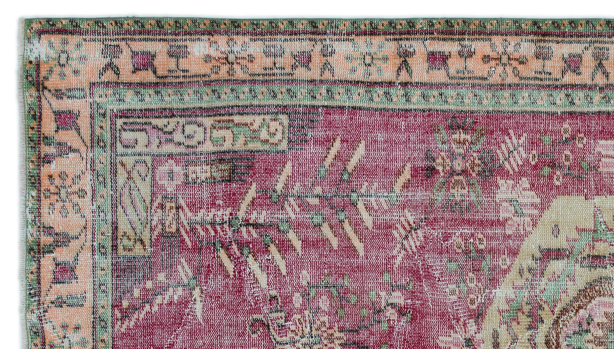 Magenta and peach vintage-style rug with a distressed geometric border and traditional floral motifs.