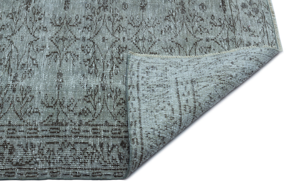 Grey and brown distressed vintage-style rug with a floral medallion pattern, shown with a corner folded over.