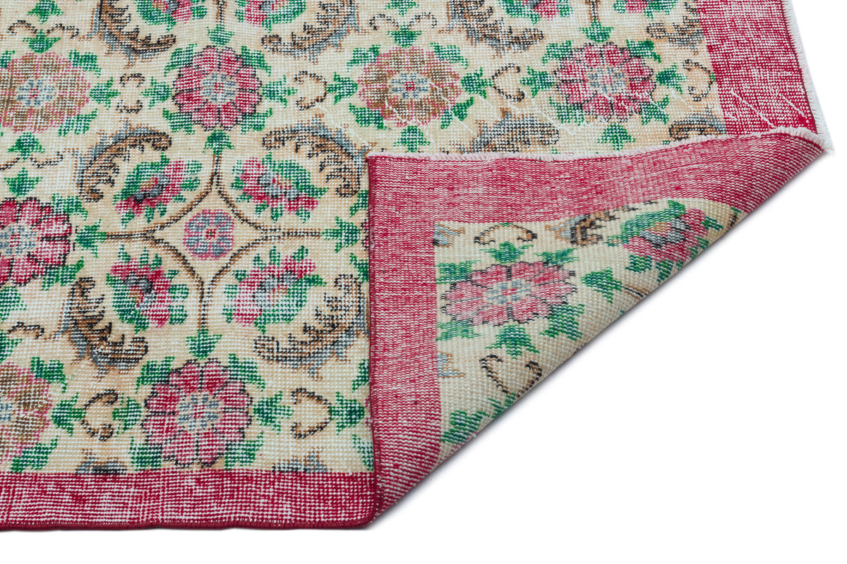 Cream rug with a floral medallion pattern in red, green, and brown, featuring a folded corner on a white background.