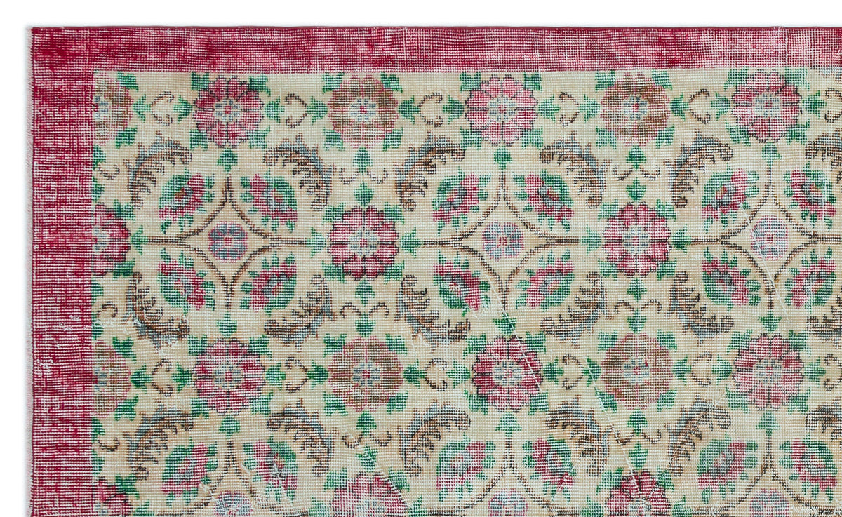 Cream rug with a red border and a repeating floral medallion pattern in red, green, and brown.