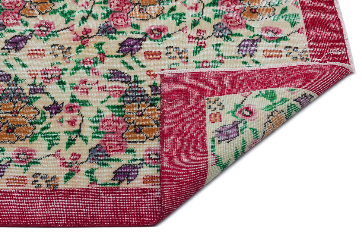 Cream rug with a floral pattern in pink, purple, and green, featuring a wide red border and a folded corner.